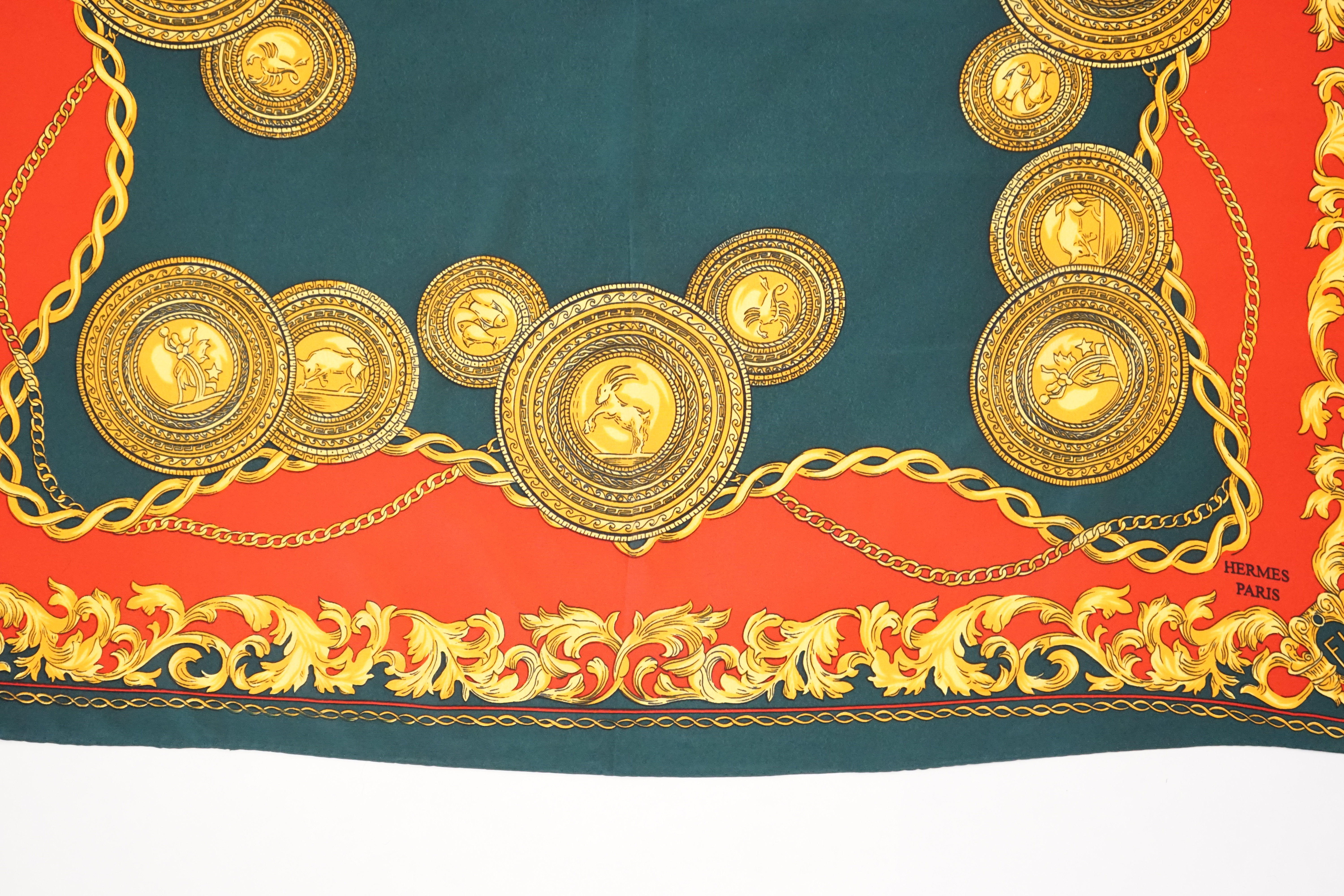 A Hermès silk scarf decorated with gold zodiac sign animals and hybrids, gold foliage and chain design around the edges, 90 x 84cm